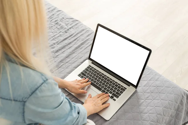 Retrato de mujer de mediana edad usando su computadora portátil de pantalla en blanco mientras está sentada espalda con espalda en el sofá en casa. — Foto de Stock