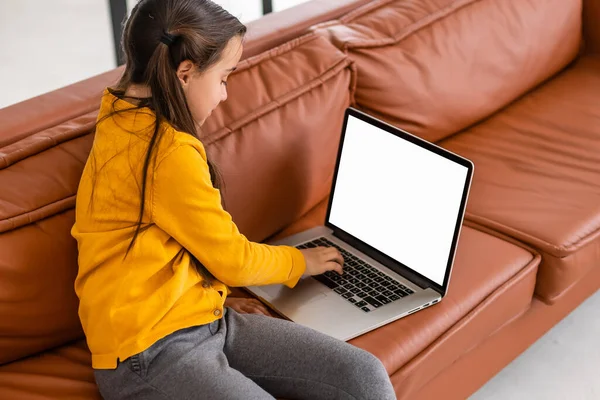 Fernstudium. Mockup-Bild von kleinen Mädchen mit Laptop mit leerem Bildschirm zu Hause, Online-Studium mit Computer, weibliches Kind am Schreibtisch in der Küche sitzen und auf Tastatur tippen, Rückansicht — Stockfoto