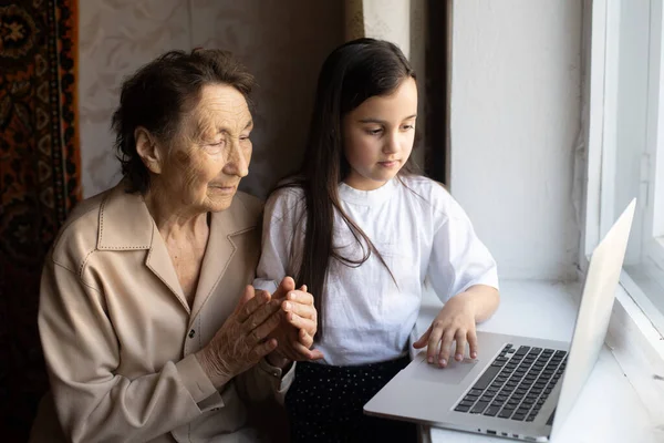 Happy senior woman sitting with her granddaughter looking at laptop making video call. Mature lady talking to webcam, doing online chat at home during self isolation. Family time during Corona — Stock Photo, Image