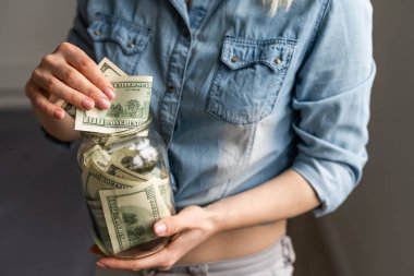 İş, finans, tasarruf, bankacılık ve insan konsepti - kadın ellerinin kapanışı bize dolar parayı cam mason kavanozuna koyar