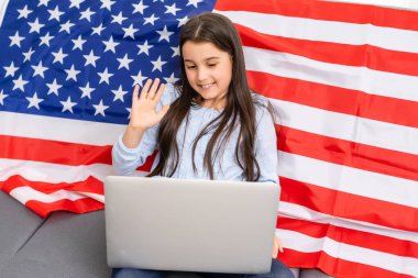 Çevrimiçi okul eğitimine dönelim. İngilizce konuşmak zor oluyor. Bilgisayarda ödev yapan bir çocuk. Öğrenci, dizüstü bilgisayarında Amerikan bayrağı üzerinde çalışıyor. Öğretmen uzaktan öğretiyor..