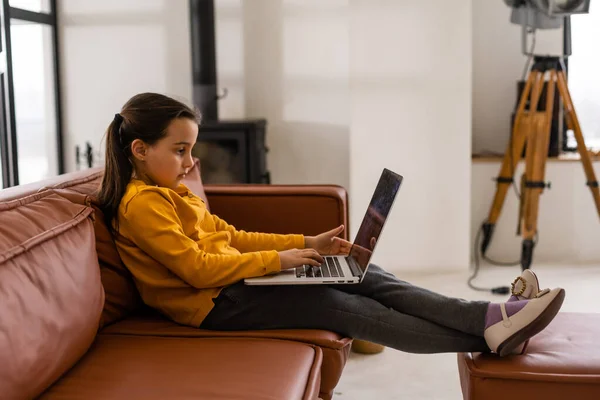 Akıllı küçük kız oturma odasında ödevini yapıyor. Oturuyor ve Laptop kullanıyor.. — Stok fotoğraf
