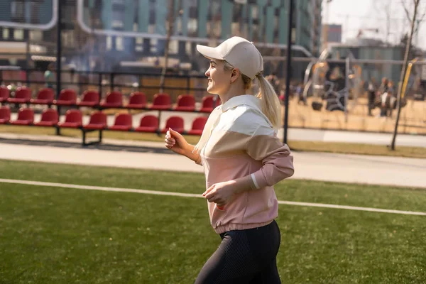 Młoda piękna blondynka fitness dziewczyna robi rozciąganie na stadionie. aktywność sportowa. Zielony stadion trawa na tle. — Zdjęcie stockowe