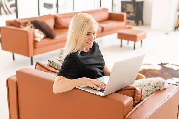 Ευτυχισμένη περιστασιακή όμορφη γυναίκα που εργάζεται σε ένα φορητό υπολογιστή κάθεται στο σπίτι. — Φωτογραφία Αρχείου