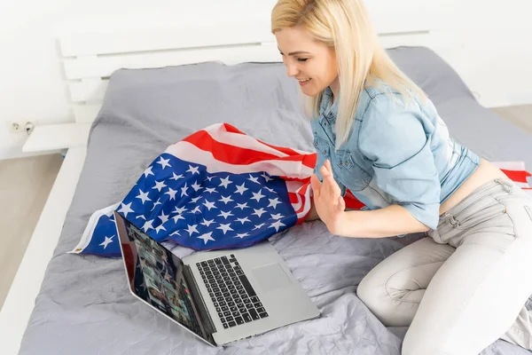 Americká mladá dívka živě streamuje se svým laptopem. V pozadí vlajka USA. Koncept Vloggeru. — Stock fotografie