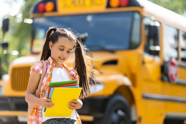 Malá dívka stojící u velké školní autobus dveře se svým batohem. — Stock fotografie