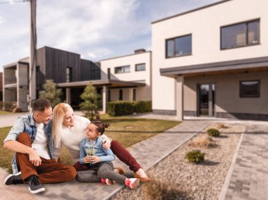 Mutlu bir aile. Yeni bir evin arka planında bir aile. Arka planda modern yeni ev var..