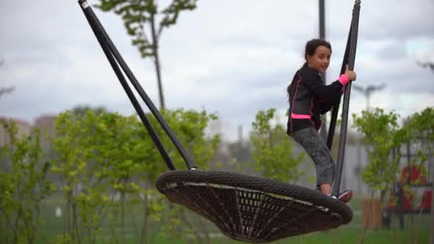 Una ragazzina che gioca al parco giochi. Bambino felice che si arrampica sulla rete da gioco, cavalca un'altalena e bungee, stile di vita attivo — Video Stock