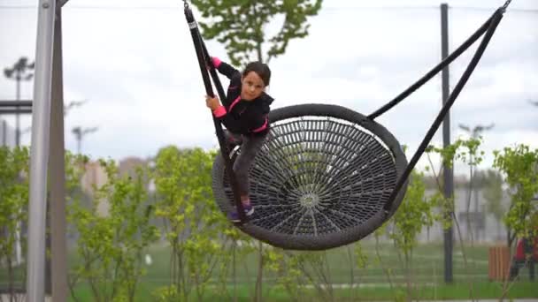 Meisje dat op de speelplaats speelt. Gelukkig kind klimmen op speeltuin net, paardrijden een schommel en bungee, actieve levensstijl — Stockvideo