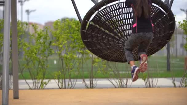 Meisje dat op de speelplaats speelt. Gelukkig kind klimmen op speeltuin net, paardrijden een schommel en bungee, actieve levensstijl — Stockvideo