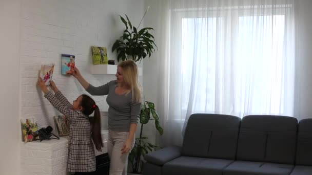 Eine junge und attraktive Familie hängt Fotoleinwand an eine weiße Wand — Stockvideo