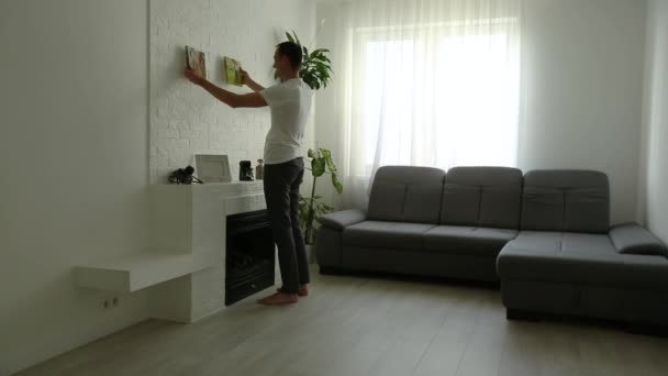 Молодой человек висит холсты на стене дома — стоковое видео