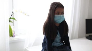 Virüse karşı tıbbi maske takan hasta küçük kız kameraya yakından bakıyor. Salgın hastalık, kendini izole etme, ev karantinası, salgın, koronavirüs.