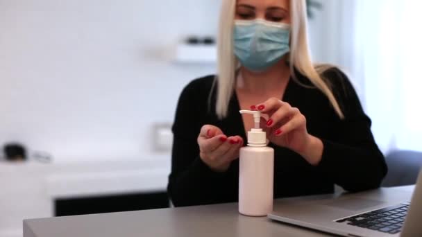 在covid-19检疫期间，一名戴着防护医疗面罩的年轻女自由职业者在家里远程工作。把消毒剂放在桌子上。卫生概念. — 图库视频影像