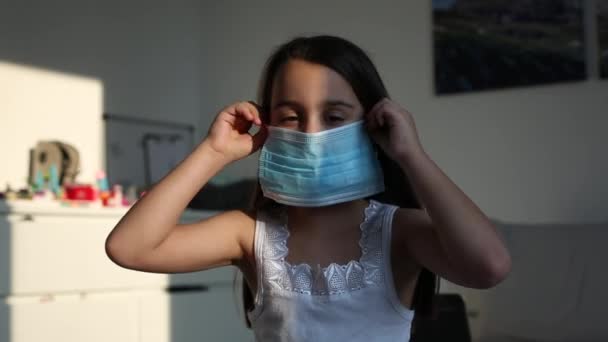 La petite fille porte un masque protecteur contre le coronavirus et diverses infections - quarantaine, maladie. La fille enlève son masque protecteur et se réjouit à la fin de la pandémie — Video