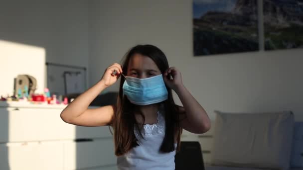 Klein meisje draagt een beschermend masker tegen coronavirus en diverse infecties - quarantaine, ziekte. Het meisje doet haar beschermend masker af en verheugt zich aan het einde van de pandemie — Stockvideo