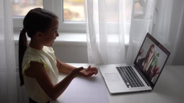 Aprendizaje a distancia de niñas de escuela primaria bastante en casa. Niño lindo enfocado escuchando lecciones de audio estudiando en la mesa, haciendo la tarea. Educación a distancia para niños sobre el concepto de cuarentena. — Vídeo de stock