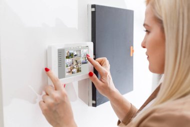 Modern evde oturan genç bir kadın akıllı ev istasyonunu kullanıyor..