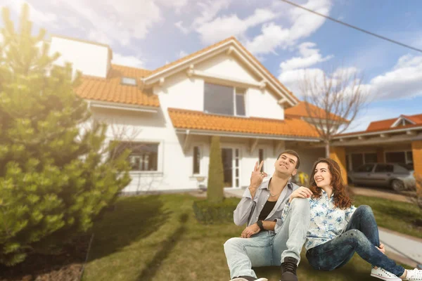 Familie sitzt auf Rasen im Hinterhof, großes modernes Haus im Hintergrund — Stockfoto