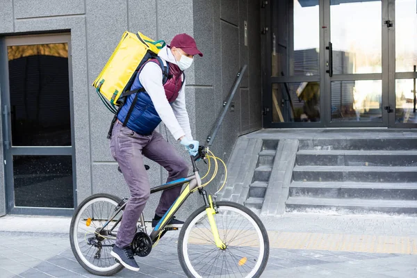 年轻的信使带着黄色的热背包运送食物，在城市骑自行车。食品交付服务概念 — 图库照片