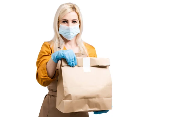 Mulher de entrega segurando um saco de papel com comida no fundo branco. entrega de comida em uma máscara protetora e luvas. Entrega detém um termômetro eletrônico e mostra que é espaço de cópia saudável — Fotografia de Stock