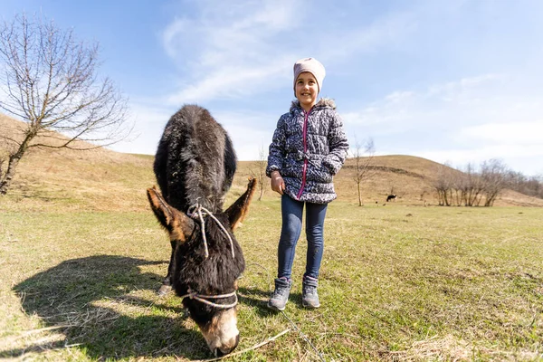 Kleines Mädchen streichelt einen Esel im Frühling — Stockfoto
