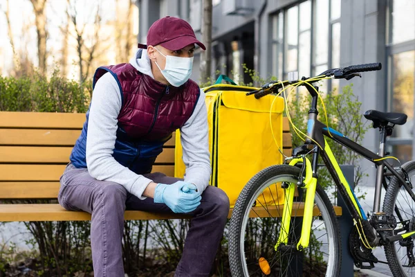 Młody kurier w masce medycznej dostarczający żywność z żółtym plecakiem termicznym, jeżdżący na rowerze w mieście. Koncepcja dostarczania żywności — Zdjęcie stockowe