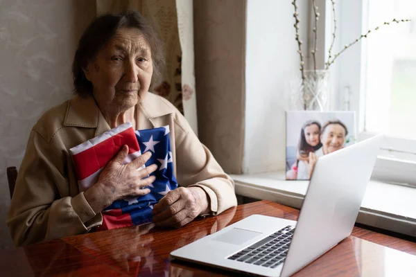 Старший, який пишається тим, що він американець, дуже стара жінка з ноутбуком і американським прапором.. — стокове фото