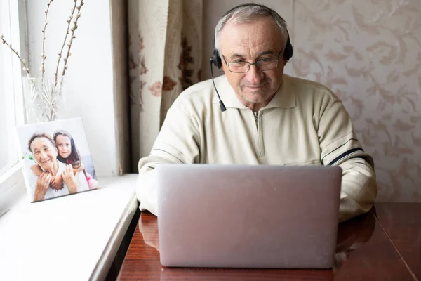 Uomo anziano utilizzando laptop e cuffie online. — Foto Stock