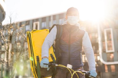Genç kurye, şehirde bisiklet süren sarı bir termal sırt çantasıyla yiyecek getiriyor. Yemek servisi konsepti