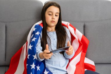 Büyük bir Amerikan bayrağı taşıyan güzel, neşeli küçük bir kızın görüntüsü.