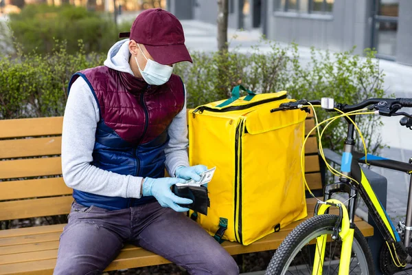 Junger Kurier in medizinischer Maske, der mit gelbem Thermalrucksack Lebensmittel ausliefert und mit dem Fahrrad in der Stadt unterwegs ist. Konzept für Essenslieferdienste — Stockfoto