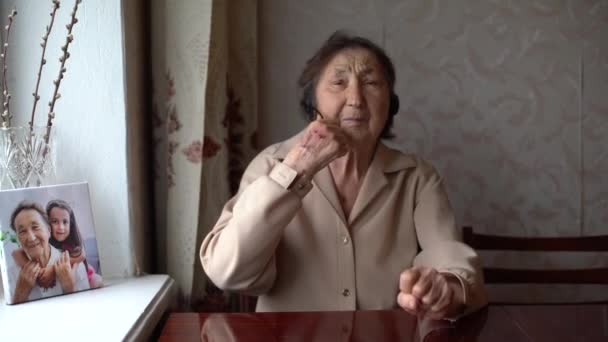 Очень старая женщина в наушниках ведет видеоразговор у себя дома. Концепция видеоразговора. headshot online. — стоковое видео