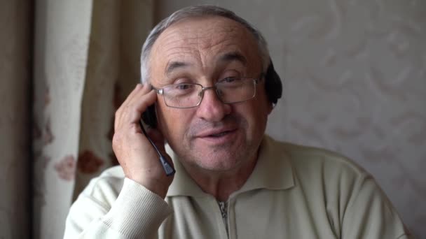 Hombre mayor sonriente usar auriculares ola a cámara que tiene videollamada en el ordenador portátil, hombre de edad avanzada feliz en los auriculares sentarse en el sofá en la charla en casa utilizando tecnologías modernas y conexión inalámbrica — Vídeo de stock