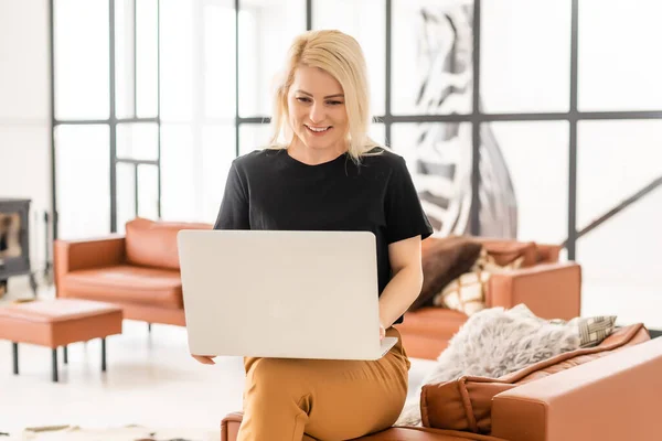Feliz mulher bonita casual trabalhando em um laptop sentado na casa. — Fotografia de Stock