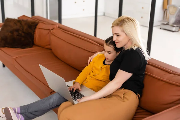 Conceito de compras online ou pagamentos. Mãe ensina sua filha usando laptop em casa. Sentado no sofá — Fotografia de Stock