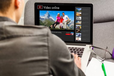 Adam gelecek seyahati planlamak için bilgi topluyor, web sitesinde internet üzerinden rezervasyon yaptırıyor, internetten bir geziyle ilgili video seyrediyor.