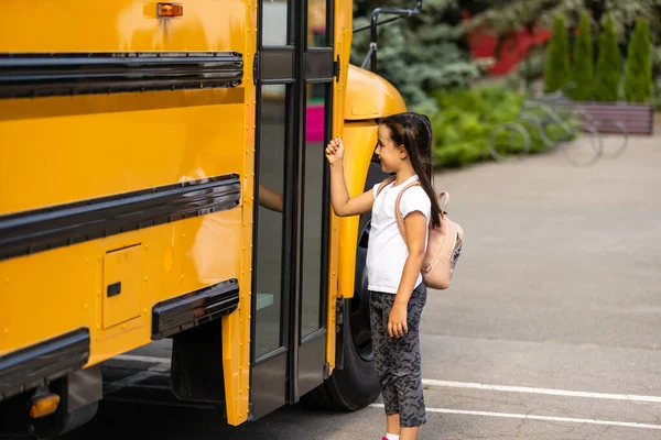 Chica con mochila cerca de autobús escolar amarillo. Transporte para estudiantes — Foto de Stock