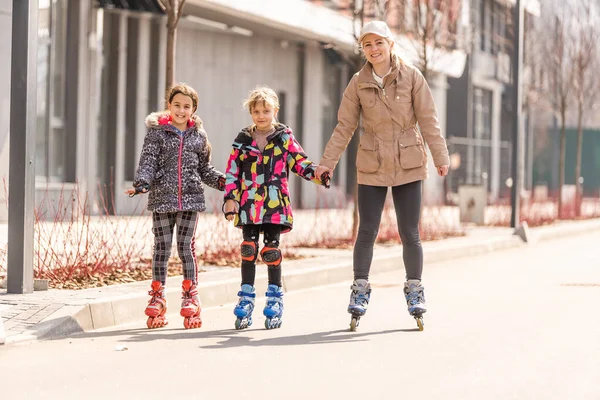 Een gelukkig gezin in rolschaatsen, moeder twee en twee dochters op rolschaatsen — Stockfoto