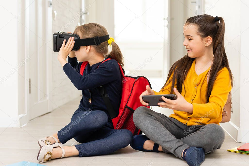 full length view of two multicultural schoolgirls holding hands while using virtial reality headsets on white background