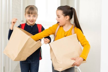 Sırt çantası ve teslimat paketleri olan iki liseli kız ellerini beyaz arka planda tutuyor.