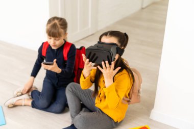 Beyaz arka planda sanal gerçeklik kulaklıkları kullanırken el ele tutuşan iki çok kültürlü kız öğrencinin tam boy görüntüsü