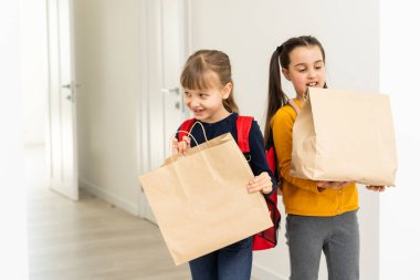 Sırt çantası ve teslimat paketleri olan iki liseli kız ellerini beyaz arka planda tutuyor.