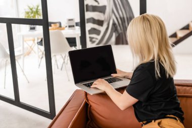 Uzaktan kumandalı ev işi, karantina sırasında serbest çalışma. Gülümseyen bayan rahat oturma odasında dizüstü bilgisayarda oturuyor ve çalışıyor.