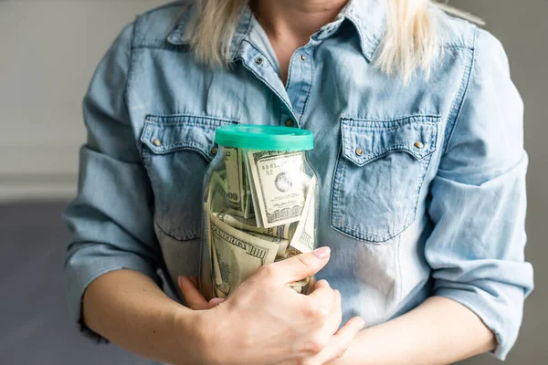 Mujer sosteniendo un frasco transparente lleno de dólares americanos. Concepto de compras — Foto de Stock
