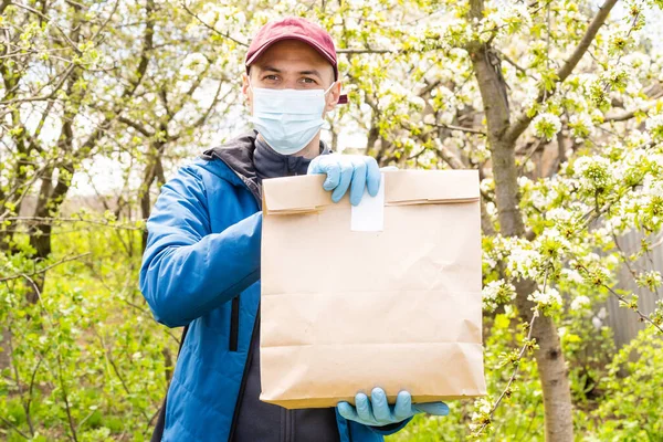 Leverans man håller papperspåse med mat på vit bakgrund, mat leverans man i skyddshandskar och skyddshandskar — Stockfoto