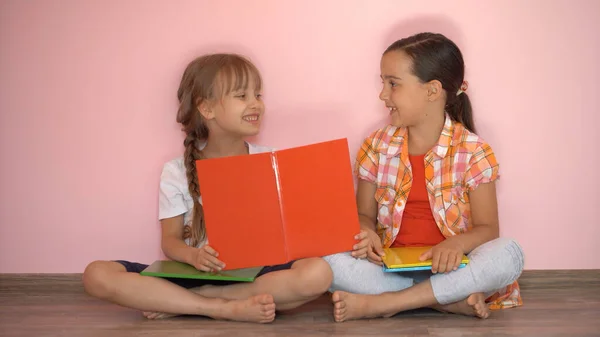 A kislányok könyvet olvasnak a nappaliban. Okos iskolás lányok csinálják a házi feladatukat suli után. Oktatás és távoktatás gyerekeknek. Magántanuló a karantén alatt. Maradj otthon szórakozni.. — Stock Fotó