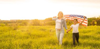 Güzel bir tarlada Amerikan Bayrağı taşıyan anne ve kızı.
