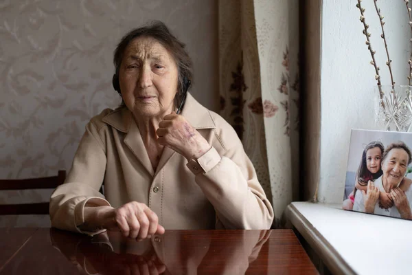 Een oude vrouw met een koptelefoon die thuis een videogesprek voert. Video conversatie concept. headshot online. — Stockfoto