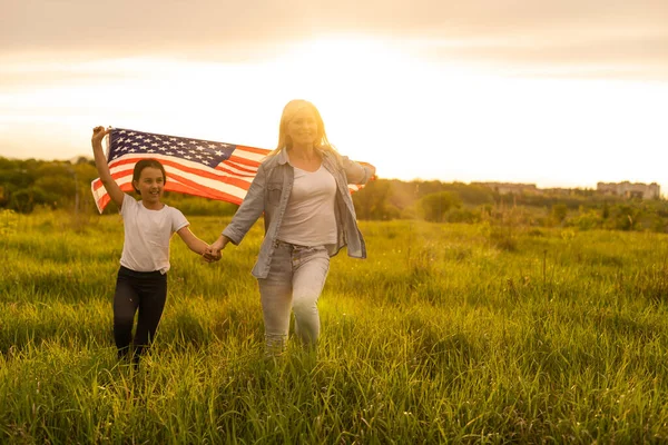 Matka a dcera s americkou vlajkou v krásném poli — Stock fotografie